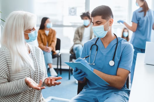 In a vibrant clinic, a nurse communicates with a senior patient while noting details on a clipboard. Others wait their turn, all wearing masks and preparing for vaccination during a health initiative. photo