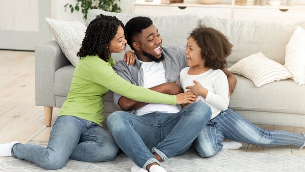 A happy black family enjoys quality time in their cozy living room, laughing and smiling as they engage in playful interaction on the floor. The warm atmosphere reflects love and togetherness. photo