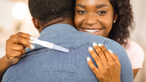 Closeup of happy african woman with positive pregnancy test hugging her husband photo