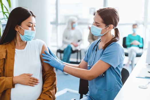 In a modern clinic, a nurse in scrubs gives a vaccine to a pregnant woman. Patients wait in the background, all wearing masks during the vaccination process for flu prevention amid a pandemic. photo