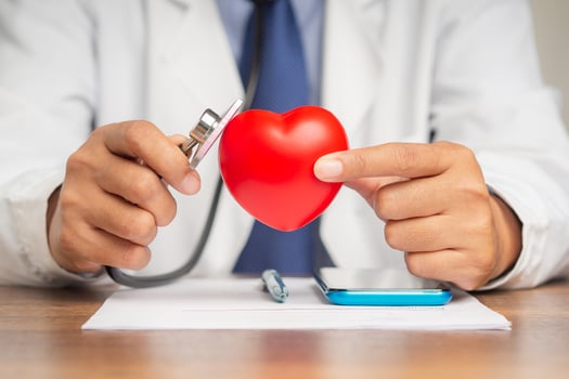 A doctor's hand holding a stethoscope checking a red heart shape symbol mockup while sitting in the hospital or clinic photo