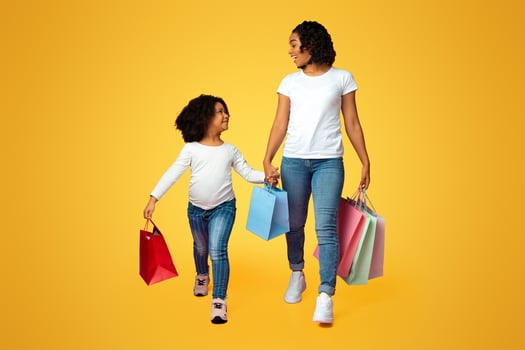 Family Shopping. Joyful African American Mother And Daughter Walking With Many Colorful Paper Bags In Studio Over Pink Background, Copy Space photo