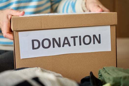 Woman holds donation box filled with clothes on bed, organizing items for charity photo