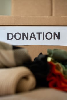 Used clothes near cardboard box labeled Donation at home photo