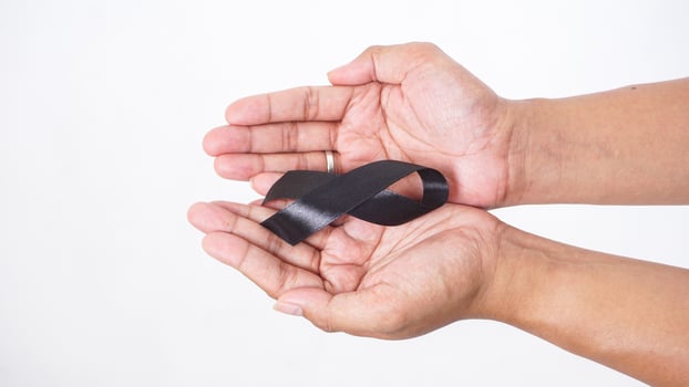 Black ribbon as mourning sign or symbol of melanoma cancer awareness in man hands isolated on white background photo