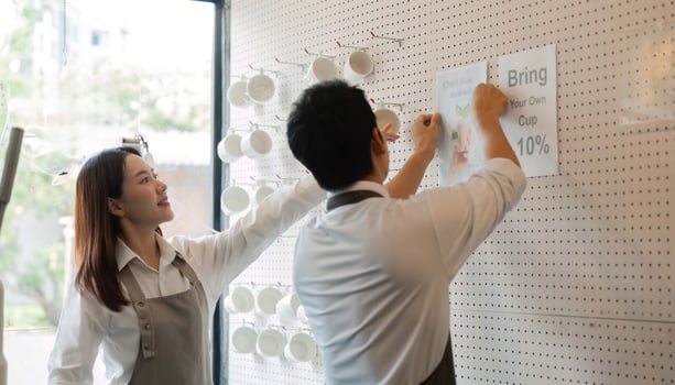 Engagement and Promotion. Two baristas hanging promotional materials for sustainability in their coffee shop, showcasing eco-friendly practices. photo