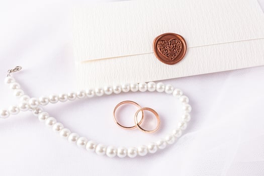 Wedding Arrangement with Wedding Rings, Pearl Beads, Envelope Invitation with Stamp on White Satin Background. top view. wedding layout, design. photo