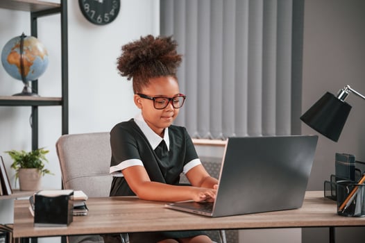 Sitting by the table with laptop. Cute female african american student child. photo