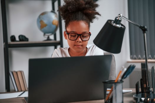 Using laptop. Cute, female african american ,student child is sitting by the table photo