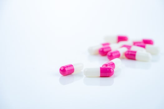 Pink-white antibiotic capsules spread on white background. Prescription drug. Antibiotic resistance in modern medicine. Healthcare and pharmaceutical industry. Medical care, pharmaceutical research photo