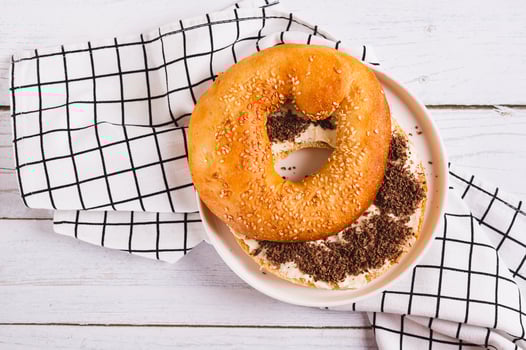 Close up of bagel sandwich with butter and grated chocolate on a plate on a table top view photo
