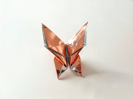 symmetrical origami butterfly crafted from shiny metallic paper in gold and silver tones featuring intricate detailed folds and a sleek modern artistic aesthetic placed on a smooth neutral surface photo