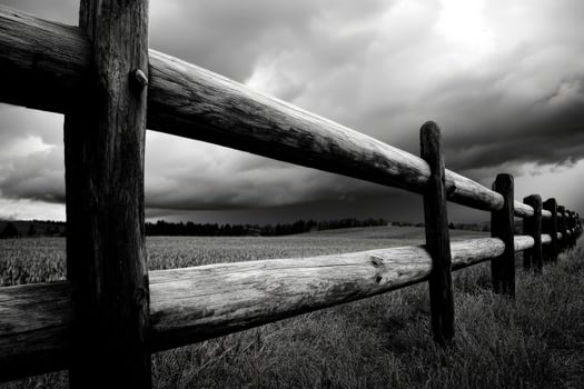 Black and white photo of a fence in front of a field
