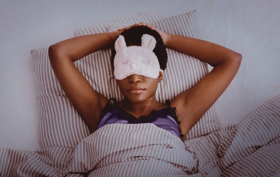 Cozy bed at night, sweet dream, rest at home and healthy lifestyle. Millennial african american female with funny mask, sleeping on bed in interior of bedroom, dark, top view, panorama, empty space photo