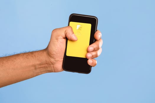 A young African American man isolates himself in a bright setting while holding a smartphone with a yellow card. The simplicity of the moment highlights modern lifestyle choices. photo