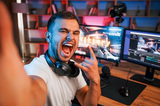 Making selfie, celebrating victory. Male game streamer in casual clothes is indoors ,with pc photo