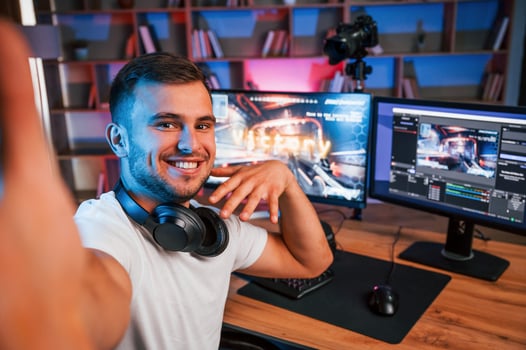 Making selfie, celebrating ,victory. Male game streamer in casual clothes is indoors with pc photo