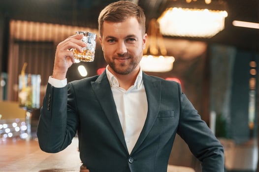 An elegant man in black suit is in the bar, tasting the alcohol drink photo