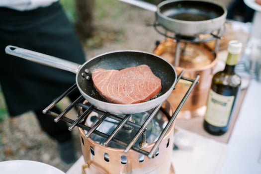 Tuna steak is fried in a frying pan with spices on a gas burner on a table in the garden photo
