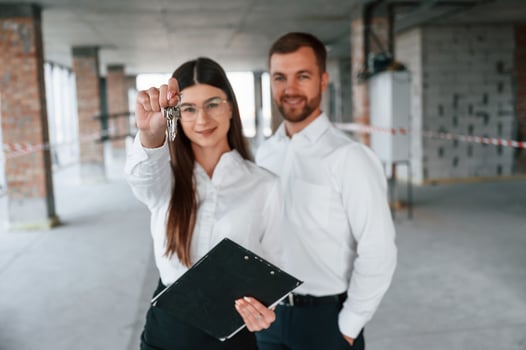 Happy young woman is receiving keys for her new home indoors. With man that is in formal clothes photo