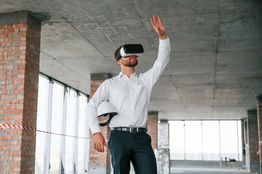 Hands raised up. Man in formal clothes, is playing VR game in the building that are on construction site photo