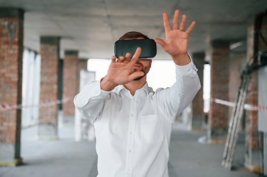 Hands raised up. Man in formal, clothes is playing VR game in the building that are on construction site photo