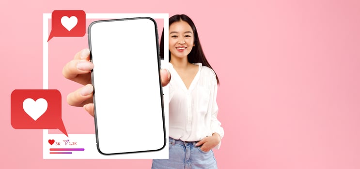 An influencer smiles while holding a blank smartphone in front of a pink background, highlighting social media engagement elements like hearts and chat bubbles, perfect for online content promotion. photo
