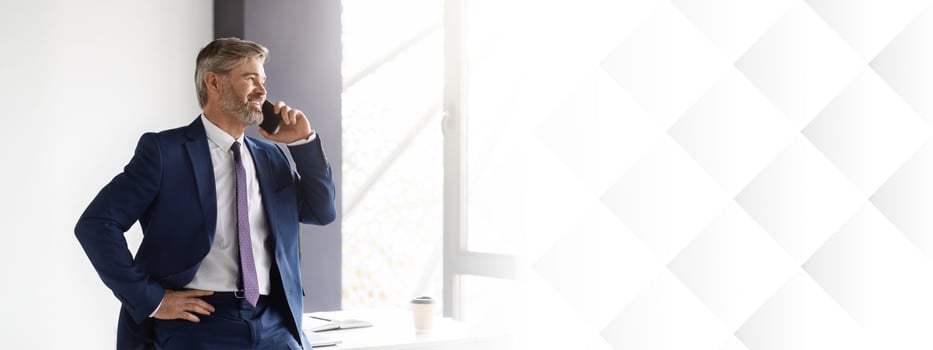 Business Call. Confident Middle Aged Businessman Talking On Cellphone At Office, Handsome Mature Man Entrepreneur Wearing Suit Standing Near Desk And Enjoying Mobile Communication, Copy Space photo