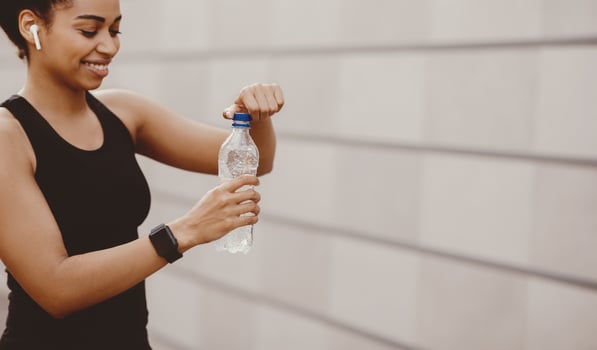 Water, healthy lifestyle and outdoor exercise. Smiling african american young woman with wireless headphone opening bottle of water, outdoors, free space photo