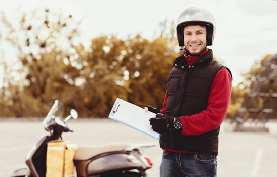 Courier Man In Uniform Offering To Sign Paper Holding Folder And Pen Standing Near Scooter Outside, Smiling To Camera photo