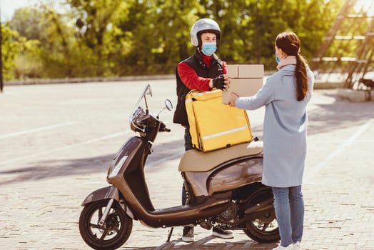 Courier Service. Delivery Man Giving Woman Food Boxes With Lunch Ordered In Restaurant Standing With Scooter, Wearing Protective Mask Outside photo