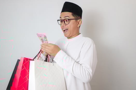 Smiling Asian Muslim man in traditional clothes holding shopping bag and money photo