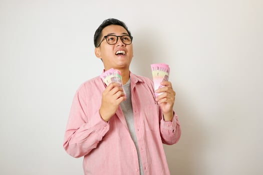Excited young handsome Asian man holding bunch of money banknotes isolated on white background photo