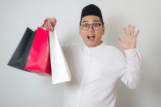 Handsome young Southeast Asian Muslim man holding shopping bags on isolated white studio background photo