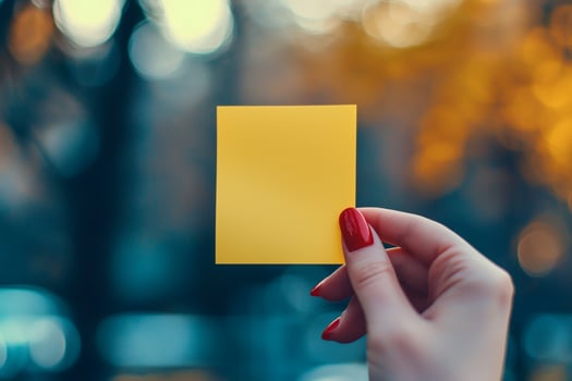 Yellow sticky note held in hand against a blurred autumn backdrop brings warmth and inspiration to the chilly afternoon photo