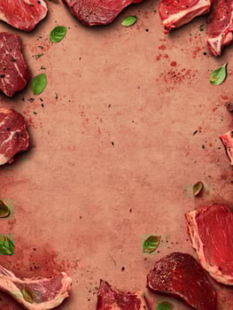 Fresh Raw Meat Steaks Arranged Around Blank Space with Basil Leaves photo