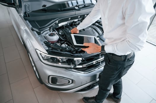 Looking ,under the hood and holding tablet. Young man in white clothes is in the car dealership photo