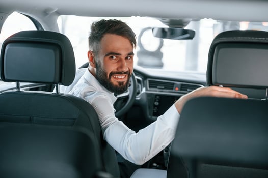 Looking, behind. Young man in white clothes is in the car dealership photo