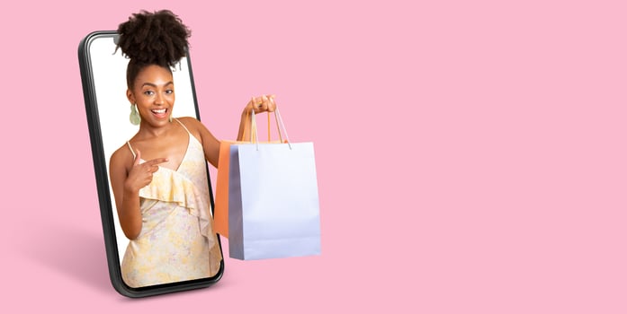 A customer is engaging in online shopping, showcasing a shopping bag while interacting with a large smartphone screen. The background is a solid pink color, providing an appealing visual contrast. photo