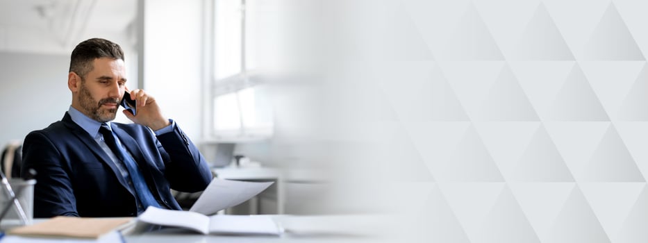 A middle aged businessman engaged in a phone call while reviewing documents in a contemporary office. He appears focused and professional, embodying entrepreneurial success and ambition, copy space photo