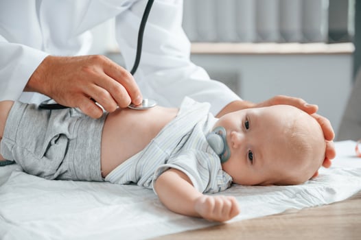 Close up view. Using ,stethoscope. Doctor in white coat is taking care of little toddler indoors photo