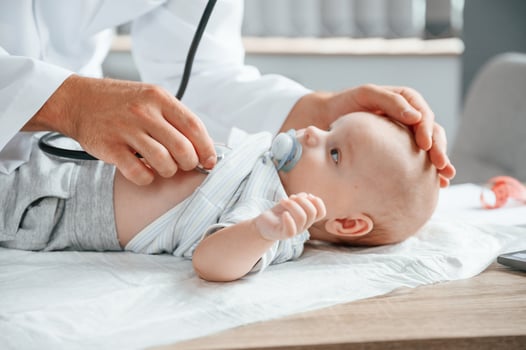 Using stethoscope. Doctor in white ,coat is taking care of little toddler indoors photo