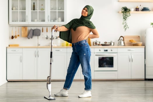 A young Muslim woman in casual attire is cleaning the kitchen floor with a steam mop. She appears confident and focused while maintaining a tidy and modern home environment. photo