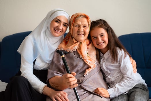 Portrait of muslim grandmother, mother and granddaughter hugging with love on the sofa smiling and looking at the camera. family of three female generations. photo