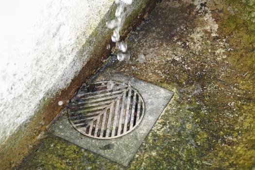 Water dripping from a wall into a metal drain on a concrete surface photo