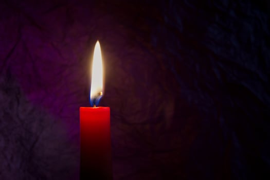 Red candle with flickering flame against a textured dark background photo