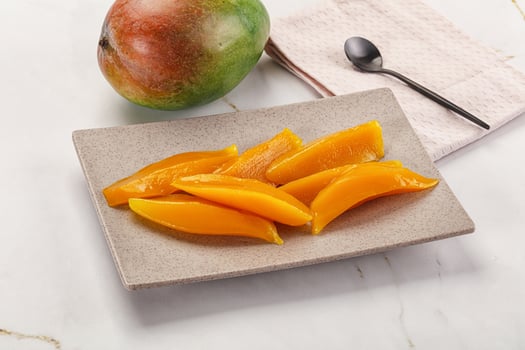 A plate of sliced mangoes and a spoon on a marble counter photo