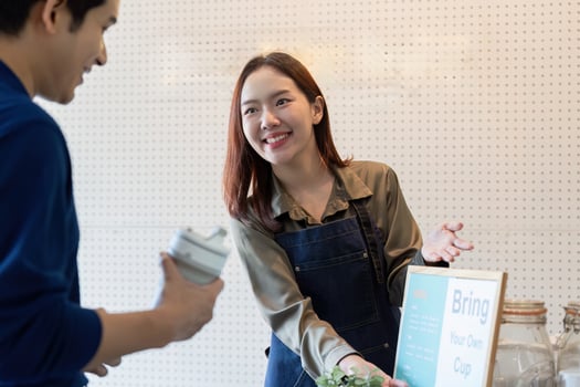 Sustainability and Customer Engagement. A barista encourages customers to bring their own cups for an eco-friendly experience. photo