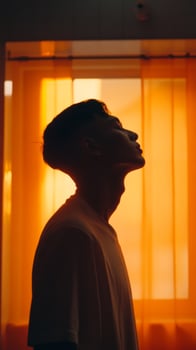 Profile of a person silhouetted against a warm orange curtain during sunset light in a cozy indoor space photo