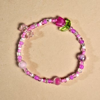 Cute pink colored beads bracelet accesories isolated on square brown cream colored background. photo